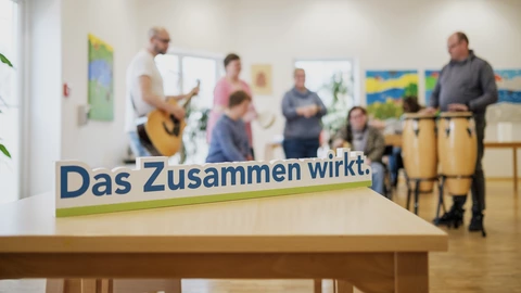 Eine Gruppe aus dem Förderzentrum musiziert zusammen. Im Vordergrund steht der Schriftzug "Das Zusammen wirkt."