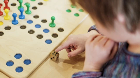 Eine Person sitzt vor einem Brettspiel und würfelt