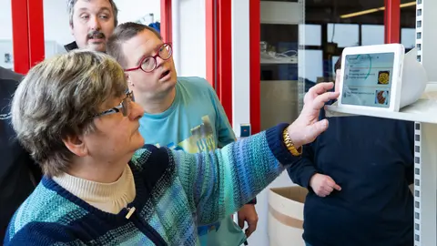 Drei Personen stehen vor der digitale Sprachassistenz Alexa. Eine Frau tippt auf den Bildschirm.