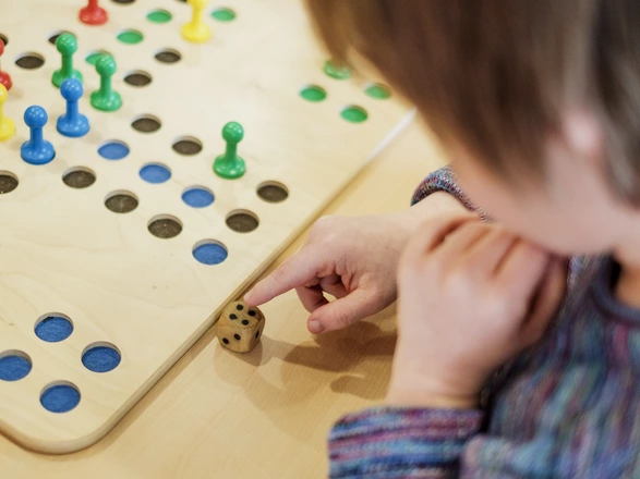Eine Person sitzt vor einem Brettspiel und würfelt.