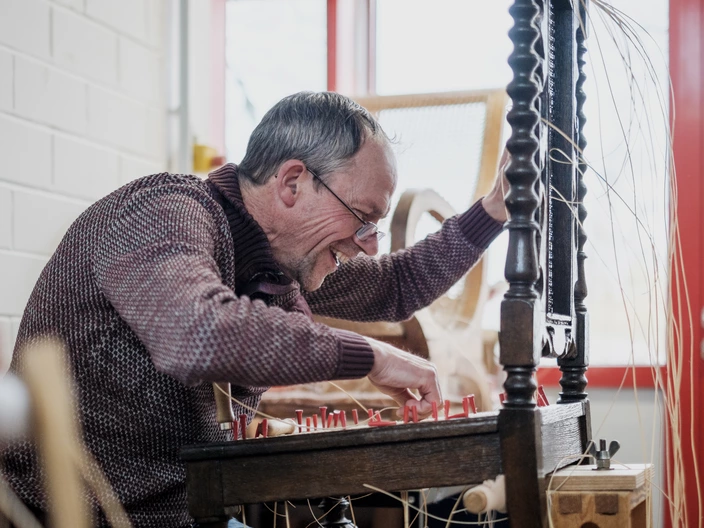 Ein Mitarbeitender der Erfurter Werkstätten flechtet eine Stuhlfläche.